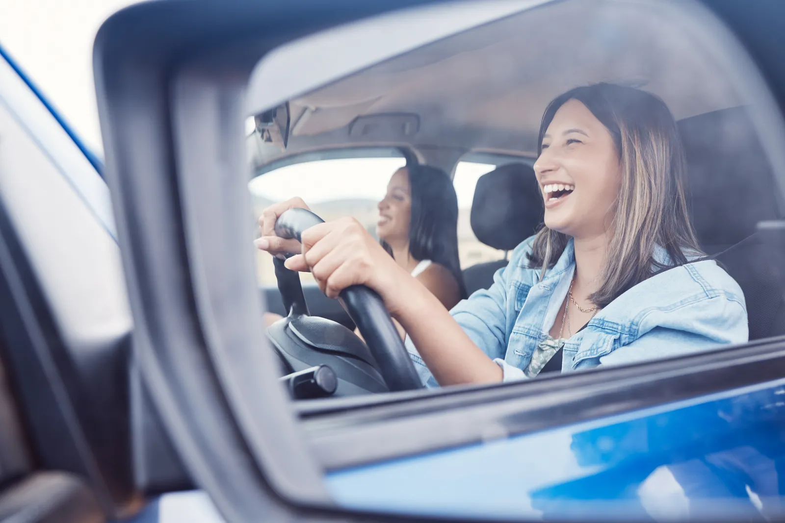 Two friends laughing in the front seats of a clean car, seen through the open driver's window